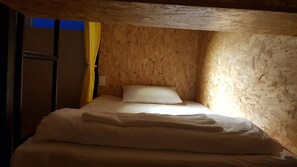 A small, cozy room with a wooden ceiling and walls, a single bed with white bedding, and a yellow curtain on a window. - White House Hostel (Nha Trang)