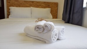 A neatly made bed with white linens and rolled towels, a wooden headboard, and a dark curtain. - White House Hostel (Nha Trang)
