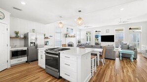 A modern kitchen with white cabinetry, a central island, and a dining area with a gray sofa and blue accents. - Private Beach, 5 BR w/awesome views, private pool & golf cart (Santa Rosa Beach)