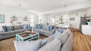 A spacious living room with a grey sectional sofa, a blue coffee table, and a ceiling fan. - Private Beach, 5 BR w/awesome views, private pool & golf cart (Santa Rosa Beach)