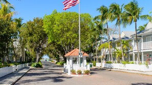 A street with a small white gazebo, a flagpole with an American flag, and a row of white buildings with balconies. - Island Oasis at the Truman Annex in Key West (Key West)