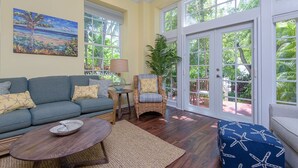 A spacious living room with a gray sofa, a round coffee table, and a wicker chair. - Island Oasis at the Truman Annex in Key West (Key West)