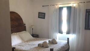 Un dormitorio con cama, mesita de noche, ventana con cortinas e imagen enmarcada en la pared.