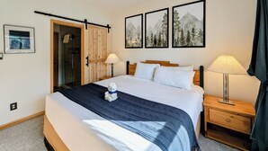 Habitación de hotel con cama, dos lámparas de noche, una mesita de noche de madera, una puerta con diseño de puerta corrediza y tres cuadros en la pared.
