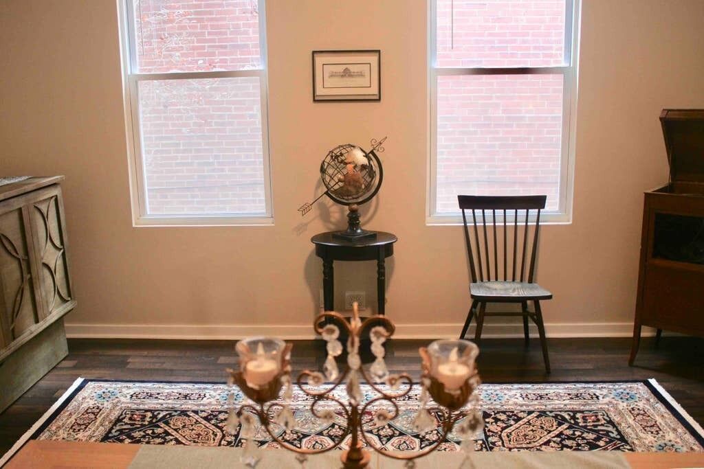 A room with a patterned rug, a globe on a stand, a chair, and a table with candles.