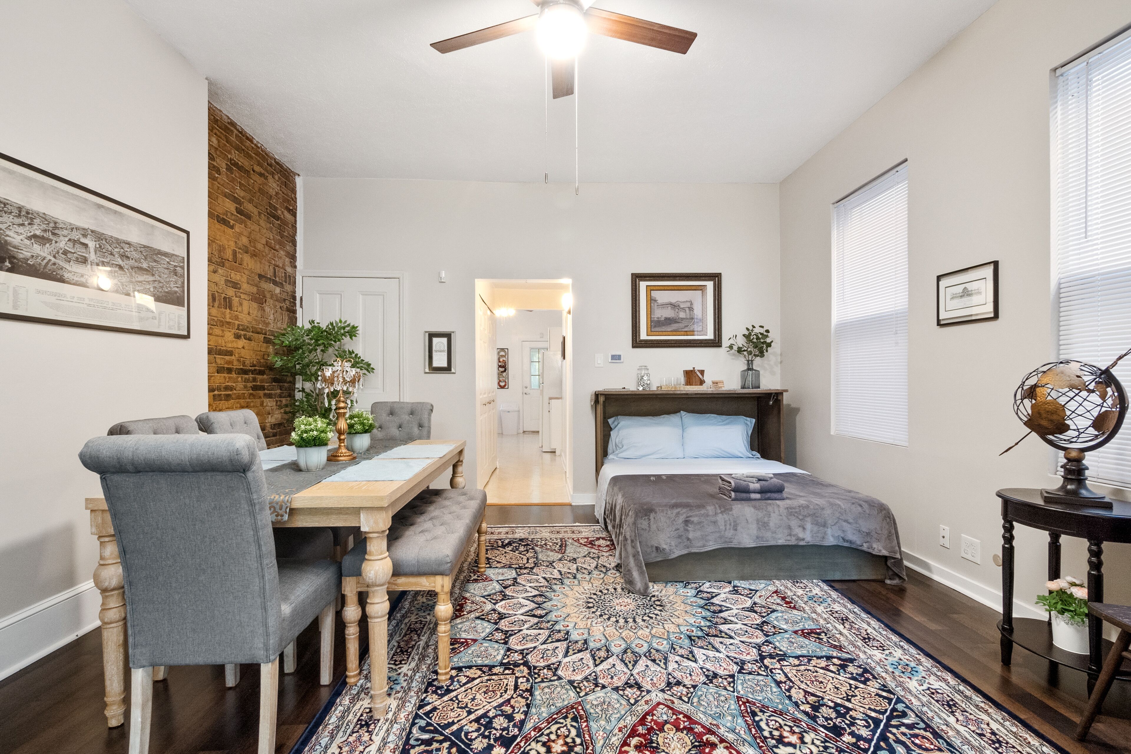 A bedroom with a bed, a desk, a chair, a rug, and a ceiling fan.