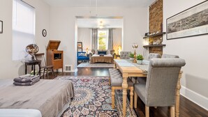 A well-lit, spacious living room with a large ceiling fan, a dining area with a wooden table and chairs, a cozy seating area with a sofa and armchairs, and a view of the city through a large window. - Centrally located in the Tower Grove East neighborhood! (St. Louis)