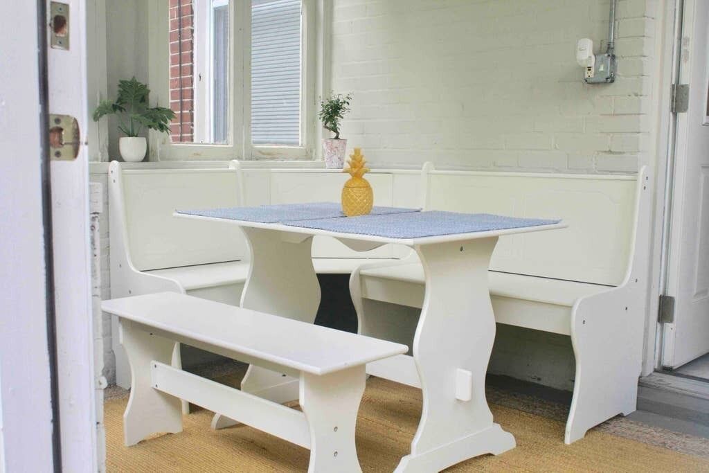 A white bench and table set in a corner with a small potted plant and a pineapple on the table.