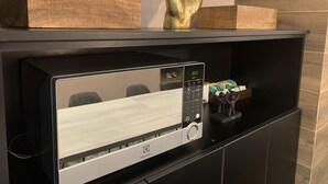 Een moderne keuken met een ingebouwde Electrolux magnetron, een houten plank met decoratieve objecten, en een zwart kastje eronder.