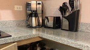 Een keuken met een koffiezetapparaat, broodrooster en diverse pannen en kookgerei, opgeborgen in een houten kast.