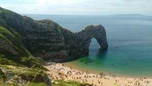 A beach with a natural rock arch formation, clear turquoise waters, and a sandy shore populated with people. - The Horse Stables (Glastonbury)