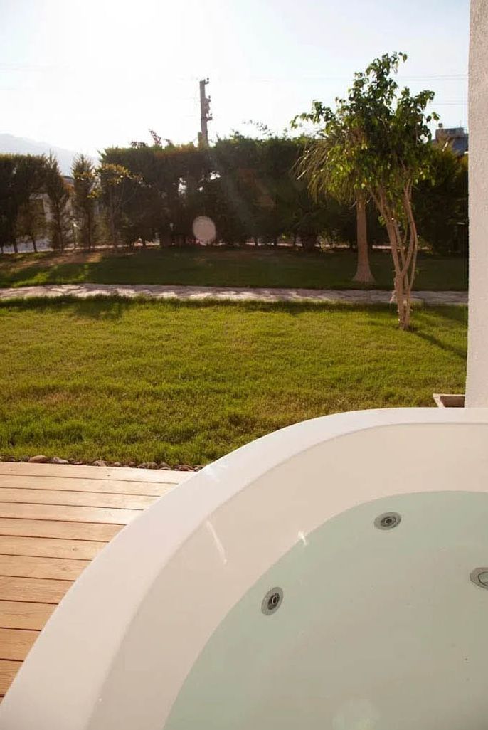 Un bain à remous sur une terrasse en bois, avec une pelouse et des arbres en arrière-plan.