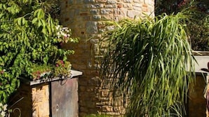 A stone tower with a metal door, surrounded by greenery and a small tree.