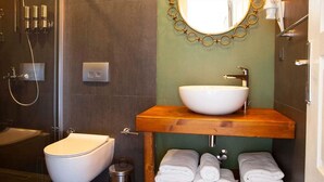 A modern bathroom with a glass-enclosed shower, a white toilet, a wooden vanity with a sink, and a mirror with a gold frame.