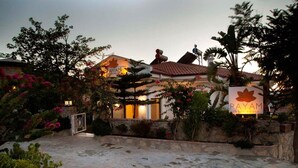 A guest house with a stone entrance, a signboard, and a well-maintained garden with flowering plants.