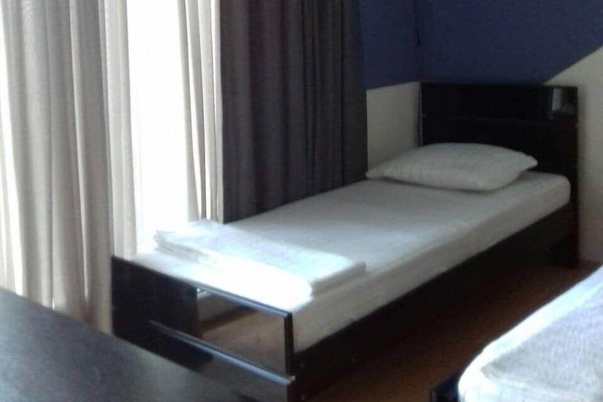 Uma cama de solteiro com colchão e travesseiro brancos, uma mesinha de cabeceira e um aparelho de ar condicionado na parede.