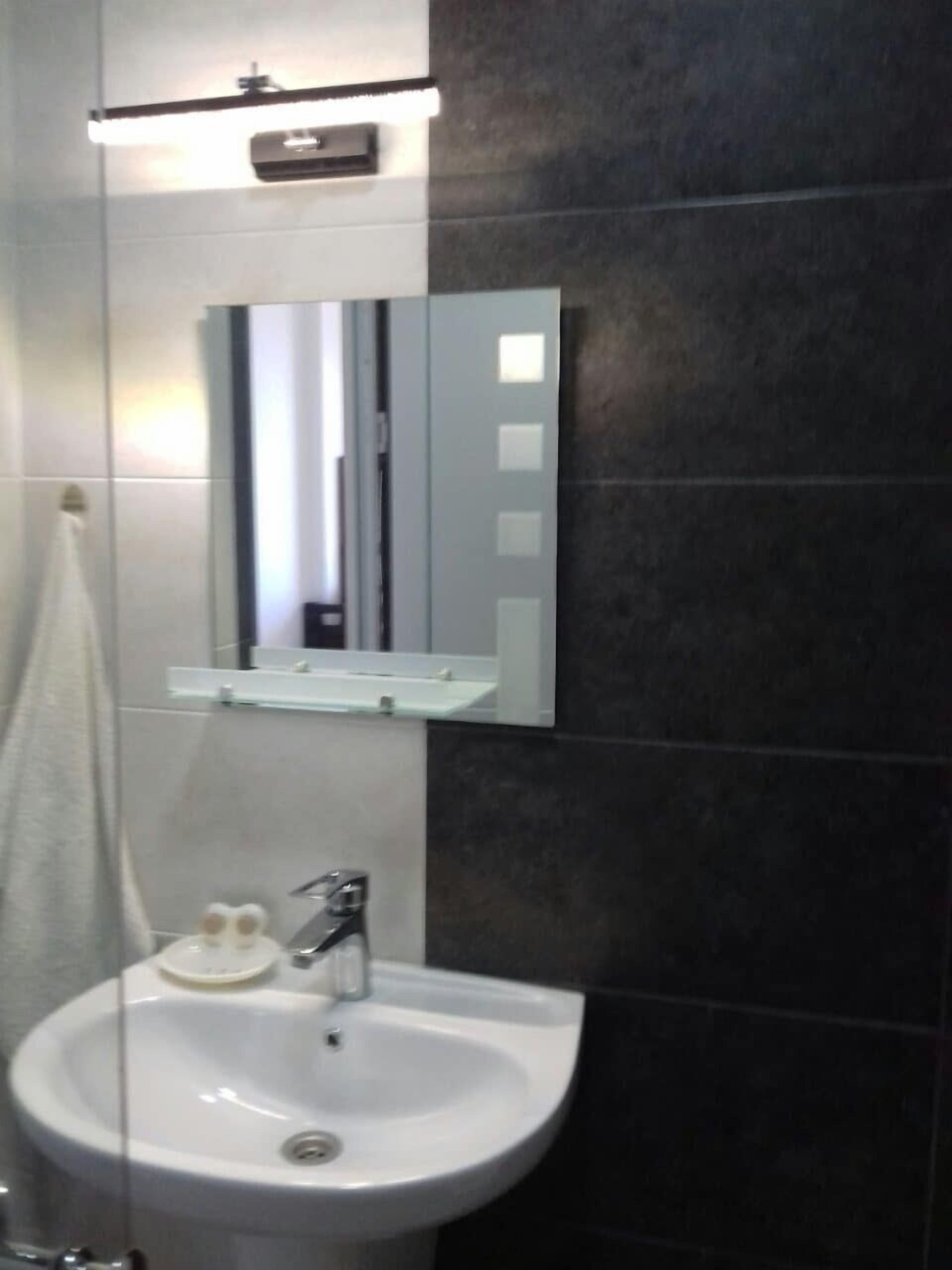 Un bagno con un lavandino bianco, uno specchio e un asciugamano appeso al muro.