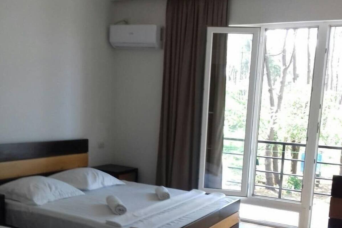 Quarto de hotel com duas camas, piso de madeira, janela com cortinas e um aparelho de ar condicionado.