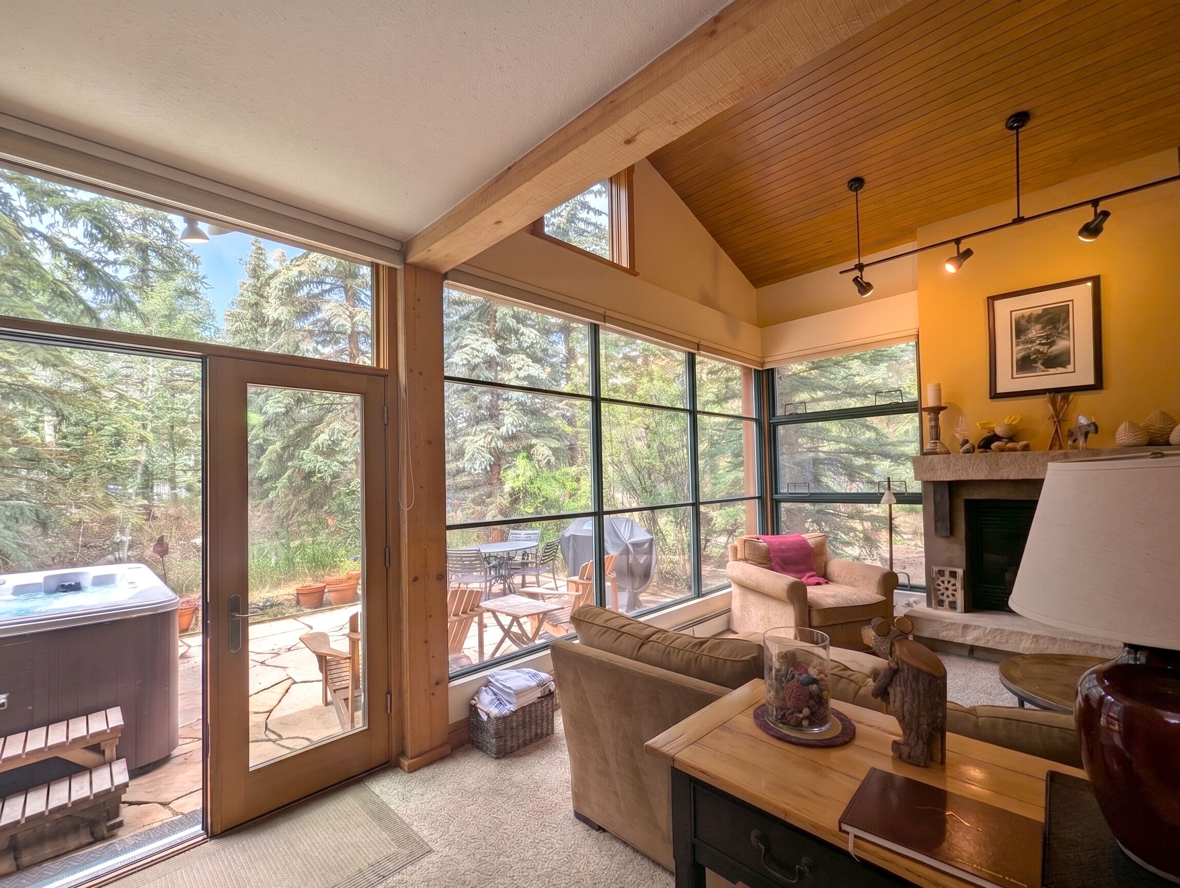 A cozy interior with a fireplace, a sofa, and a dining area with a hot tub visible through the glass doors.