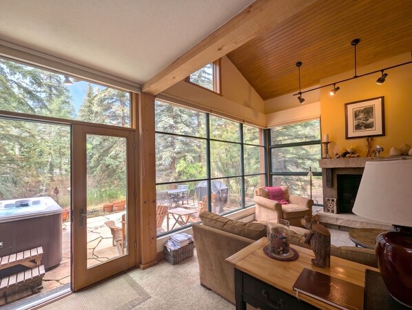 A cozy interior with a fireplace, a sofa, and a dining area with a hot tub visible through the glass doors. - Rustic & Warm Townhome with a Private Hot Tub (Keystone)