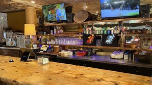 Zona de bar con mostrador de madera, dos televisores montados en la pared y diverso equipo y decoración.