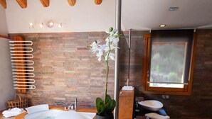 Une salle de bain moderne avec une baignoire en bois, deux lavabos, une grande fenêtre et un mur en pierre.