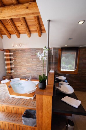 A modern bathroom with a wooden bathtub, two sinks, a large window, and a stone wall.