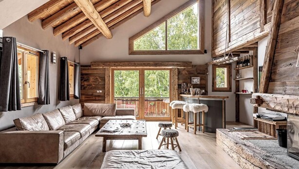 L’intérieur d’un chalet rustique est agrémenté d’un plafond en bois, d’un canapé, d’une table à manger et d’un coin cuisine avec des étagères en bois.