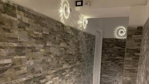 A hallway with a stone wall and marble flooring, featuring recessed lighting and a door at the end. - Popolo Relax (Rome)