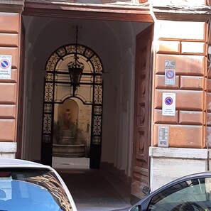 Entrada de un edificio con una puerta metálica decorativa, una señal de calle y un cartel de prohibido estacionar.