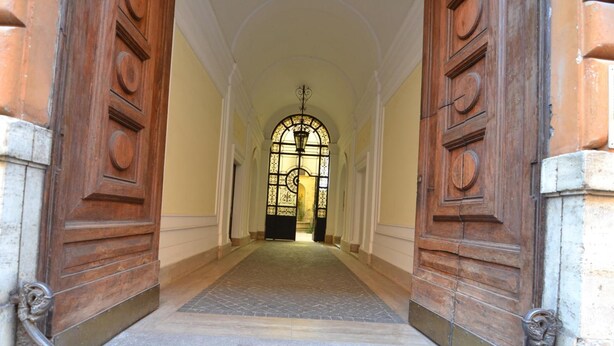 A hallway with wooden doors and a tiled floor leading to a room with a large window. - Popolo Relax (Rome)