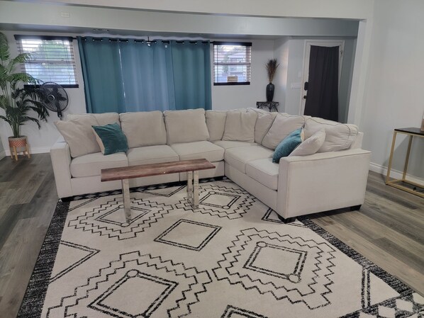 A modern living room with a beige sectional sofa, a wooden coffee table, and a patterned rug.