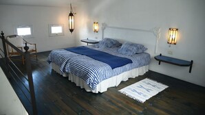 Une chambre avec un grand lit, deux tables de chevet, une chaise et un escalier.