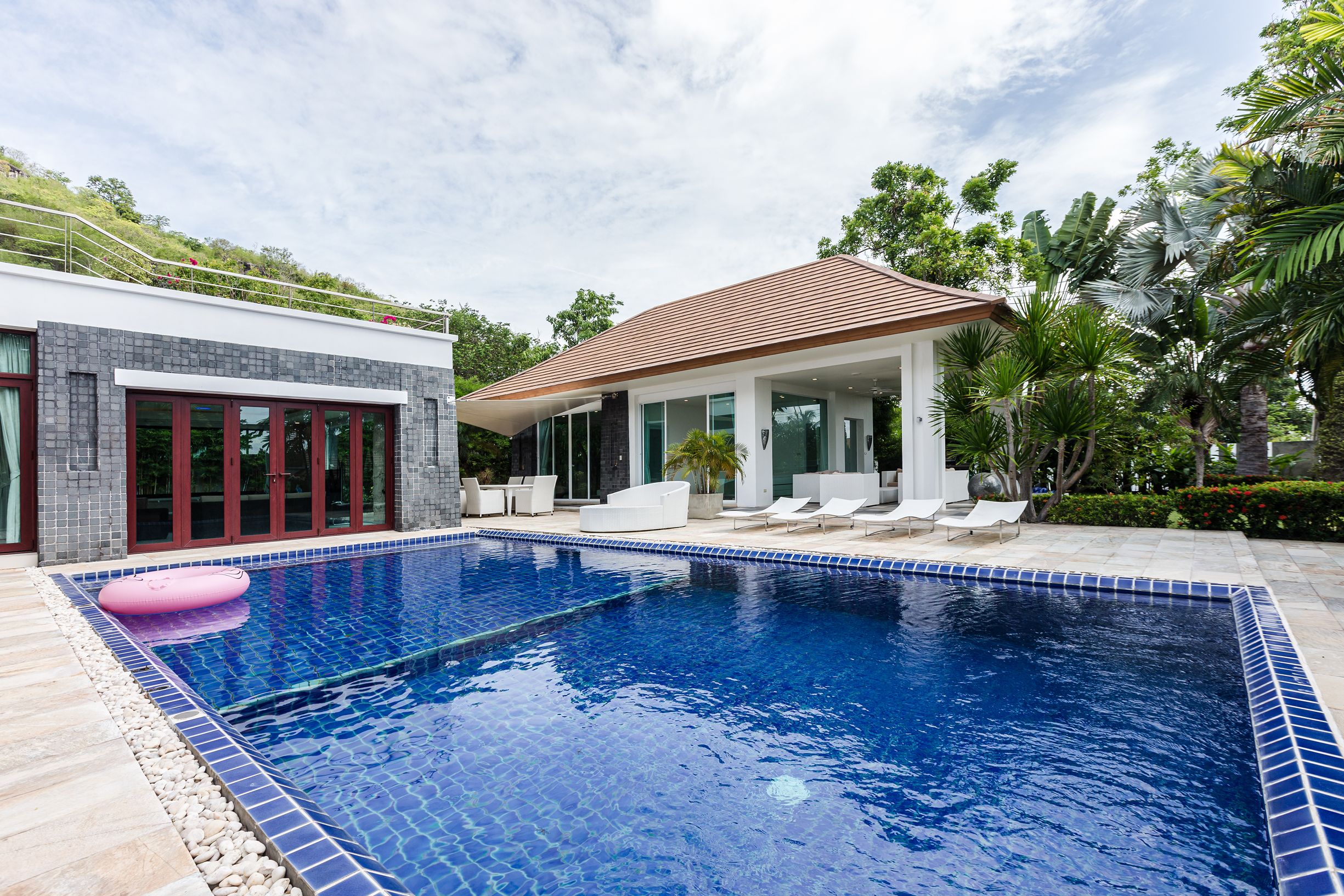 Una casa moderna con piscina, un porche cubierto y abundante vegetación.