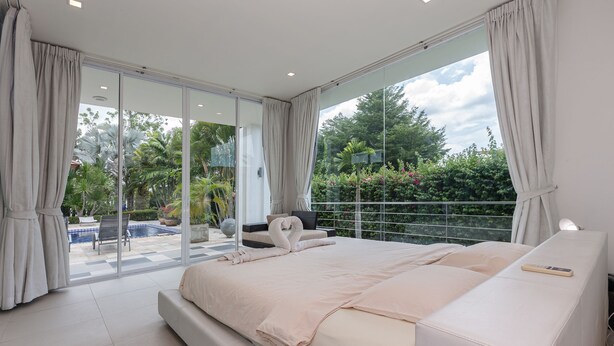 Un dormitorio moderno con una cama grande, puertas de vidrio correderas a un balcón y vistas a una piscina y vegetación.