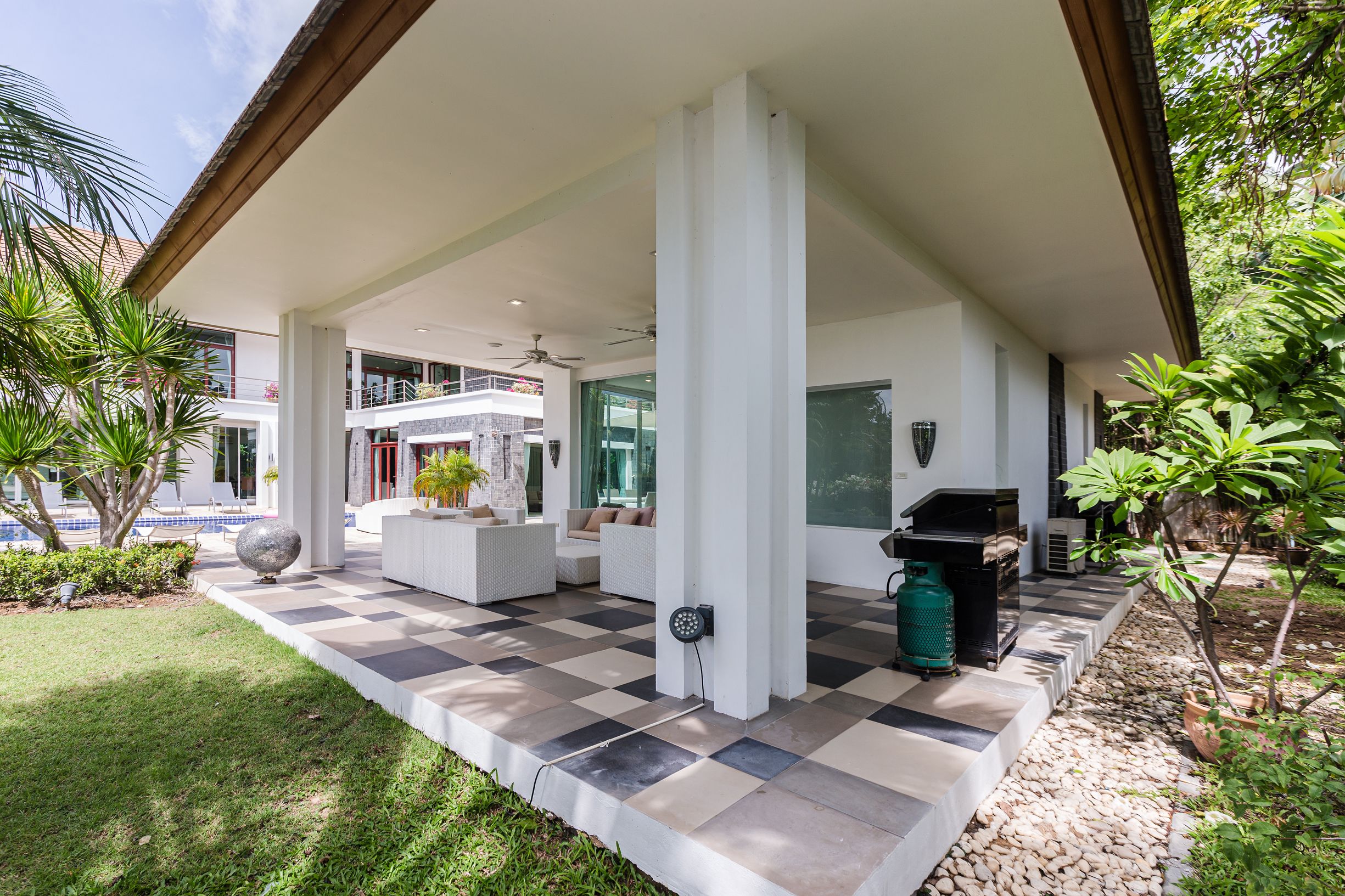 A covered outdoor area with a checkered floor, white pillars, and a grill.