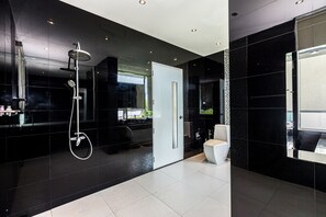 Un baño moderno con pared de azulejos negros, inodoro blanco y zona de ducha.