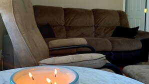 Uma sala de estar com um sofá marrom, uma vela azul em uma mesa de mármore e um abajur ao fundo.