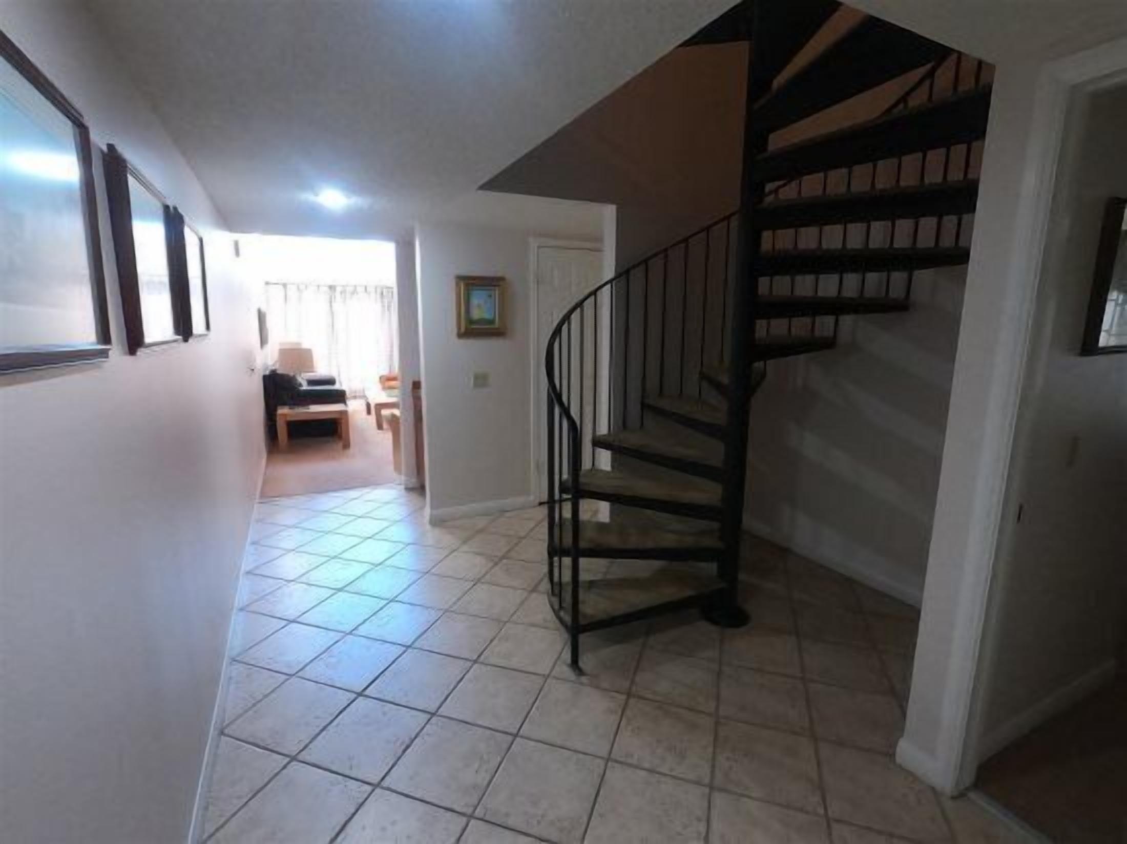 A staircase leading to an upper floor, a hallway with tiled flooring, and a door leading to a living area with a sofa and a table.