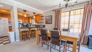 A modern kitchen with wooden cabinets, a dining table with chairs, and a large window with curtains.