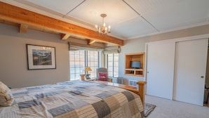 A bedroom with a large bed, wooden ceiling beams, a chandelier, a television, and a door.