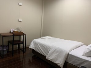 A small, clean room with a wooden desk, a chair, a bed with white bedding, and a wall socket. - Achcha - MRT Itsaraphap Station  (Bangkok)