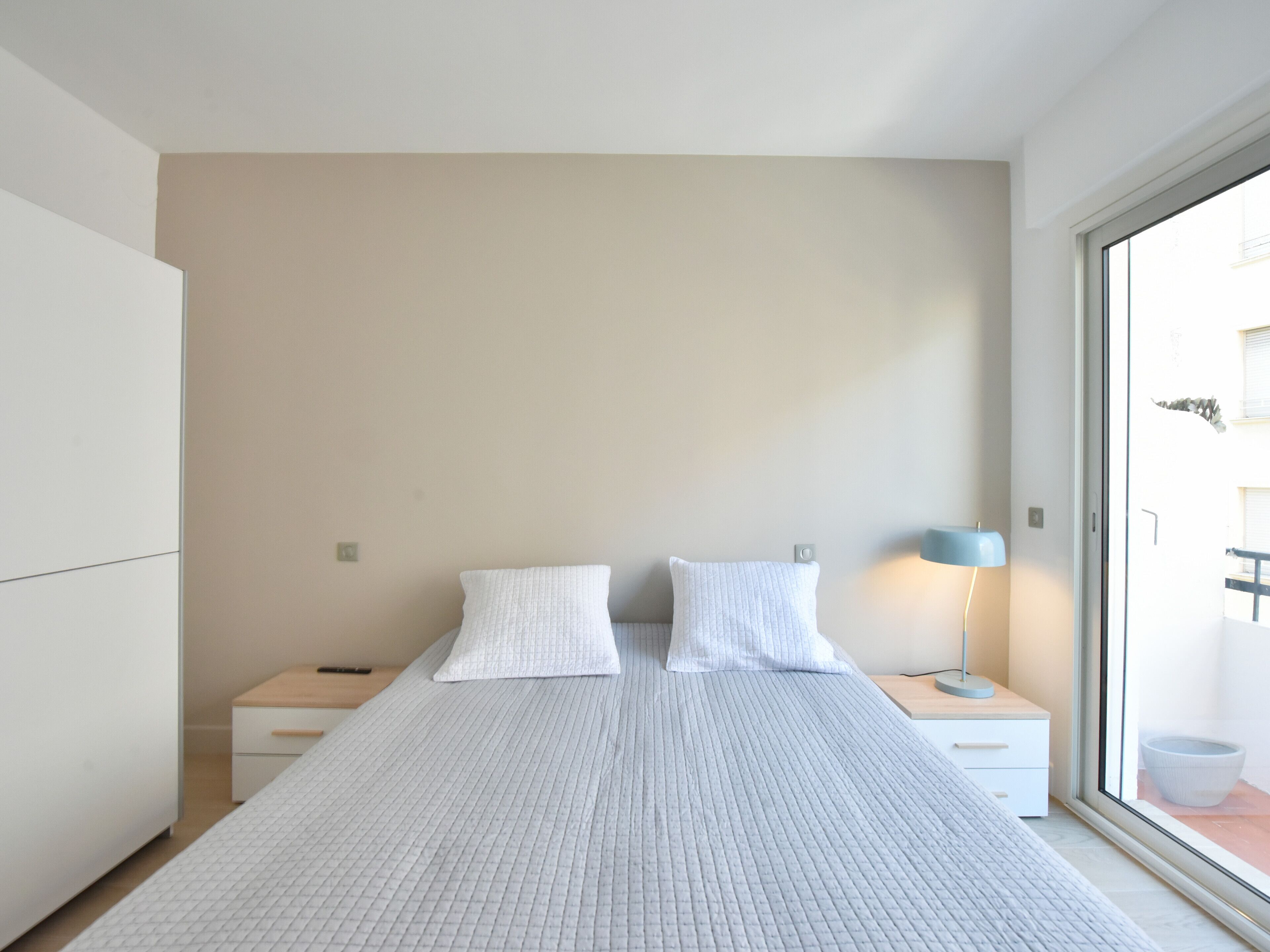 Ein modernes Schlafzimmer mit einem großen Bett, zwei Nachttischen, einem Beistelltisch und einem Fenster mit Blick ins Freie.