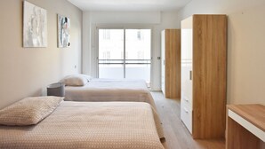 Quarto moderno com duas camas, um guarda-roupa de madeira e uma varanda com vista para a cidade.
