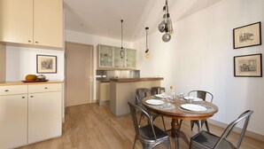 Un comedor con una mesa redonda de madera, sillas de metal y una cocina al fondo.