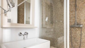 Un baño moderno con lavamanos blanco, ducha con cerramiento de vidrio y paredes con mosaicos.