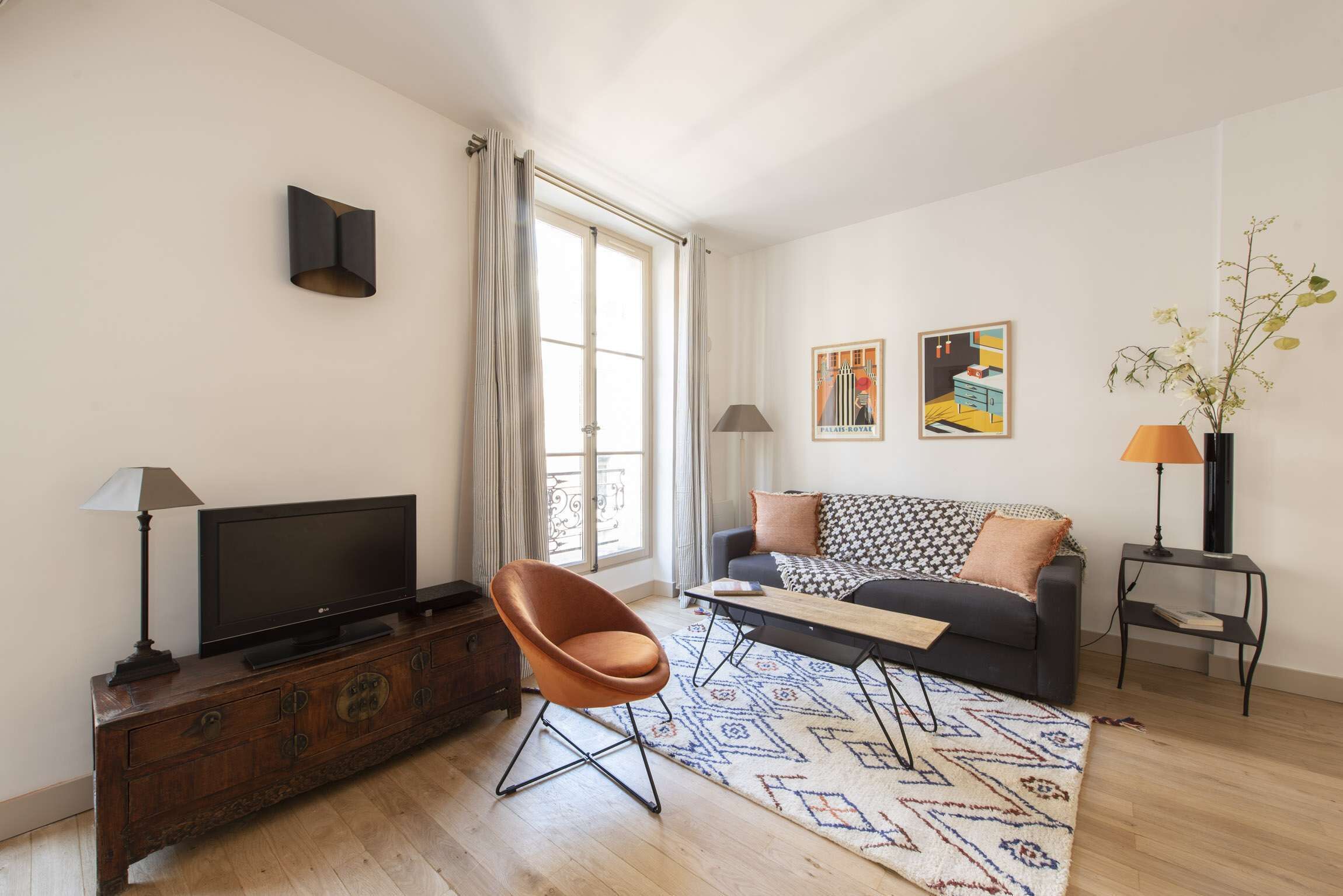 A modern living room with a sofa, a TV on a wooden cabinet, a patterned rug, and two lamps.