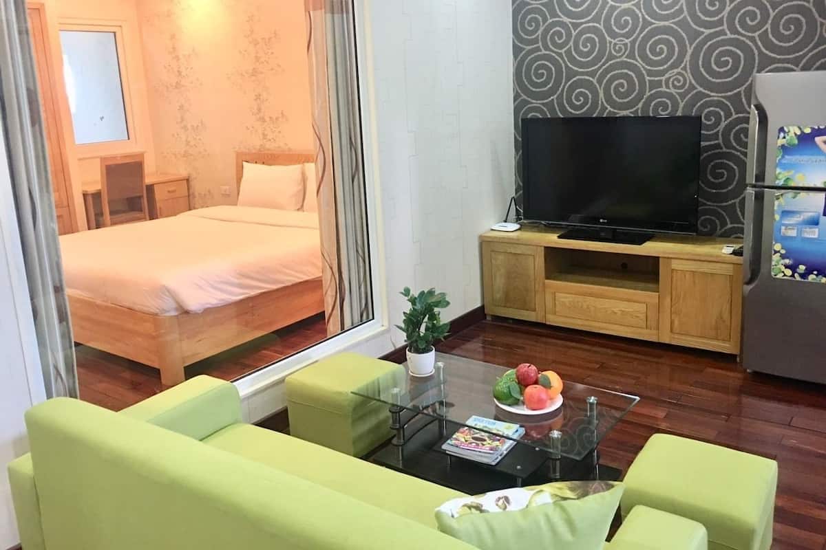 A compact living space with a bed, a television, a small dining table with fruit, and a green sofa.