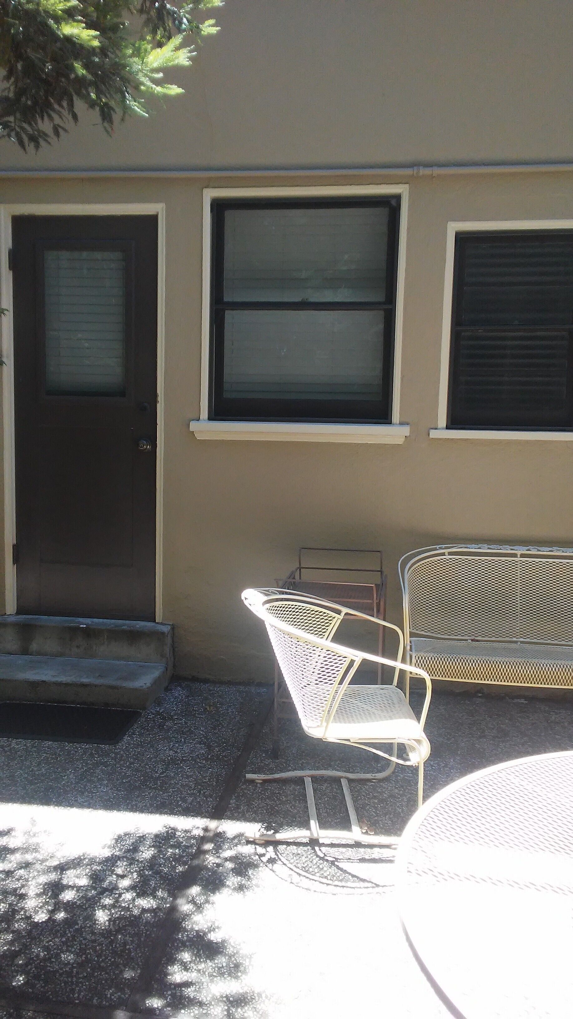 Un b âtiment avec une porte, deux fenêtres, un banc et une chaise à l’extérieur.