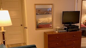 Et værelse med en blå sofa, en trækommode, et fjernsyn og et billede i ramme på væggen.